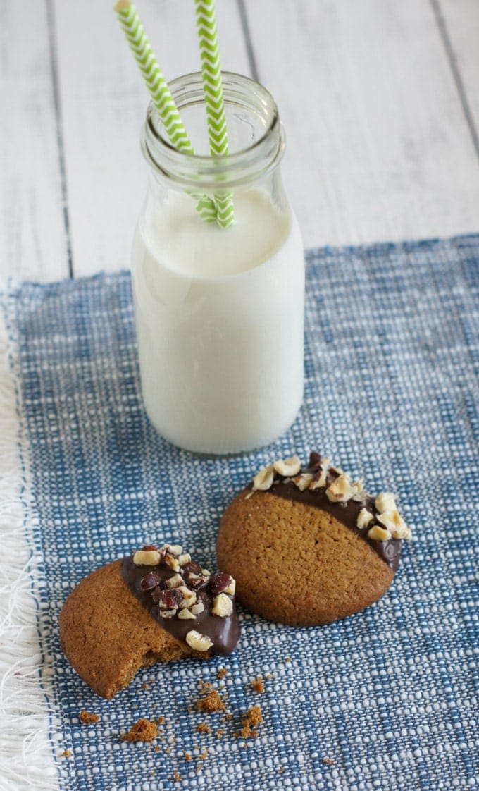 Two chocolate dipped cookies next to a bottle of milk.