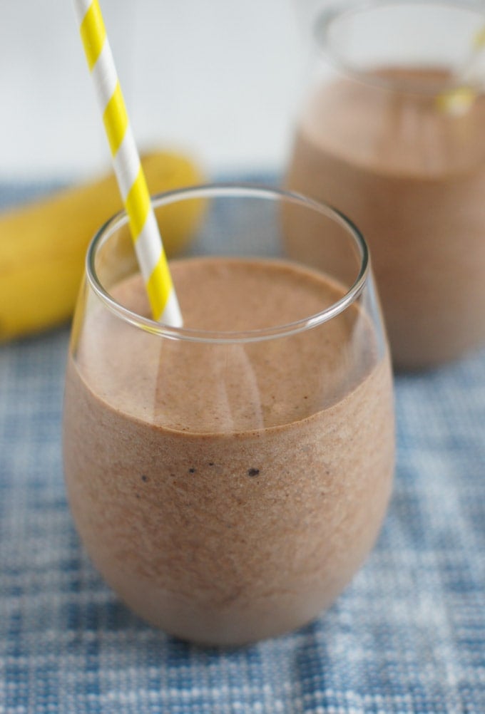 Close up photo of Banana Nutella Milkshake in a clear glass with a paper straw. 