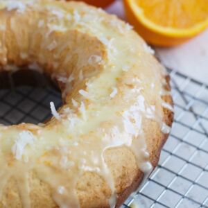 Close up of an orange ricotta coconut cake on a cooling rack.