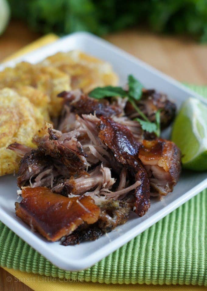 Crispy Roasted Pork Shoulder served on a white plate with a side of tostones