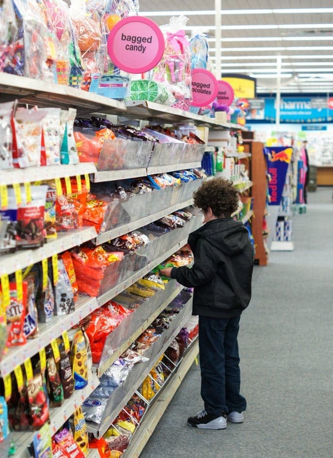 A boy standing in front of shelves at a store with candy.
