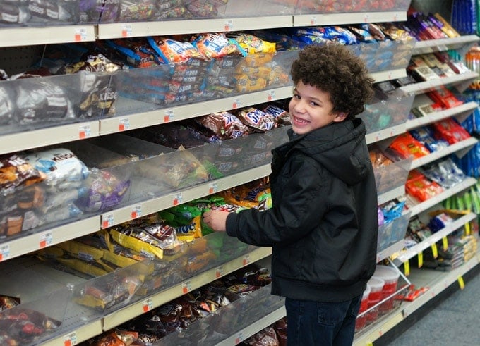 A boy picking up m&ms from store shelves.