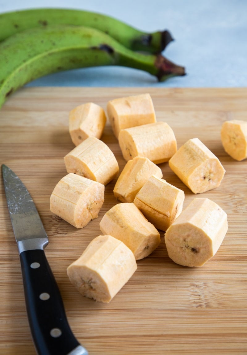 Plátanos verdes pelados y cortados en rondas de 1 pulgada en la parte superior de una tabla de madera de cocina.  