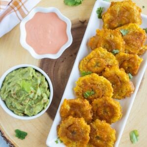 Tostones (Fried Green Plantains) served on a white plate with mayo ketchup sauce and guacamole on the side.