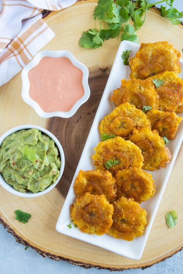 Tostones (Fried Green Plantains) served on a white plate with mayo ketchup sauce and guacamole on the side.