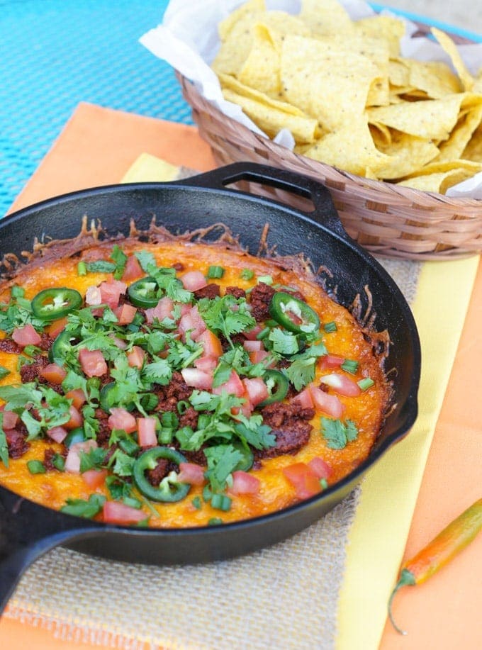 Queso fundido served in a skillet next to a basket of tortilla chips.