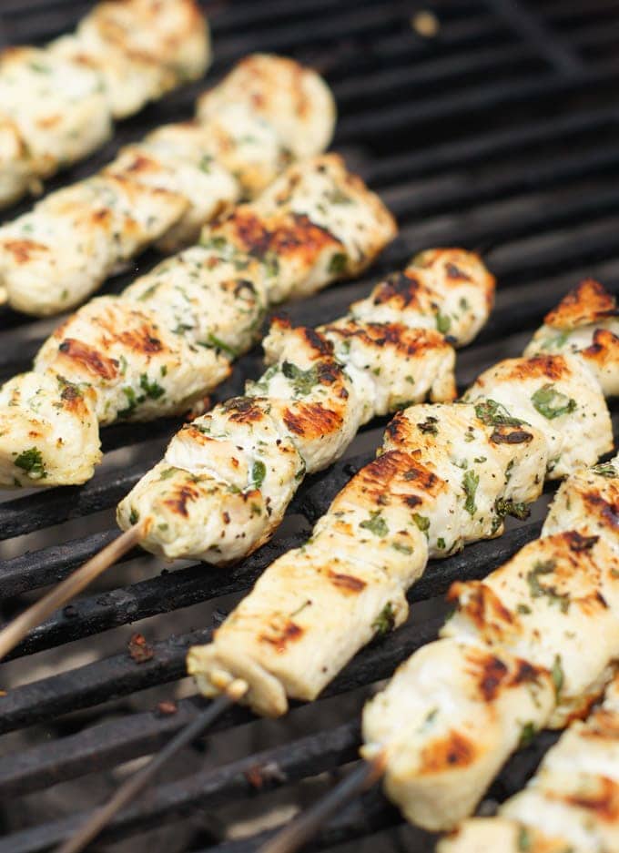 Five chicken skewers cooking on a grill.