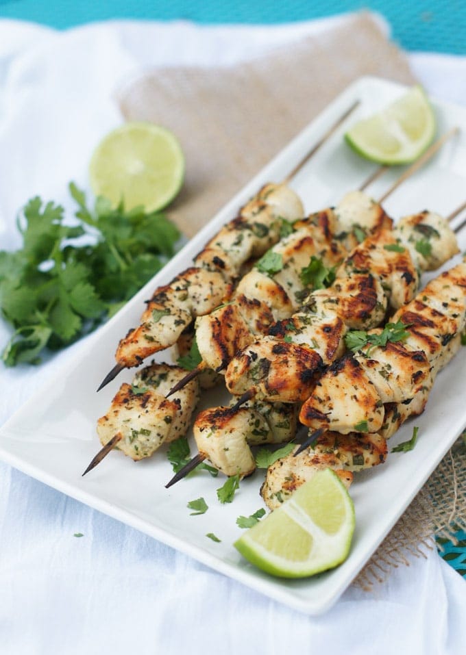 Grilled chicken skewers served with lime wedges and fresh cilantro.