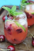 Cherry mojito served in a glass with ice and lime slices and garnished with mint.