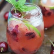 Cherry mojito served in a glass with ice and lime slices and garnished with mint.