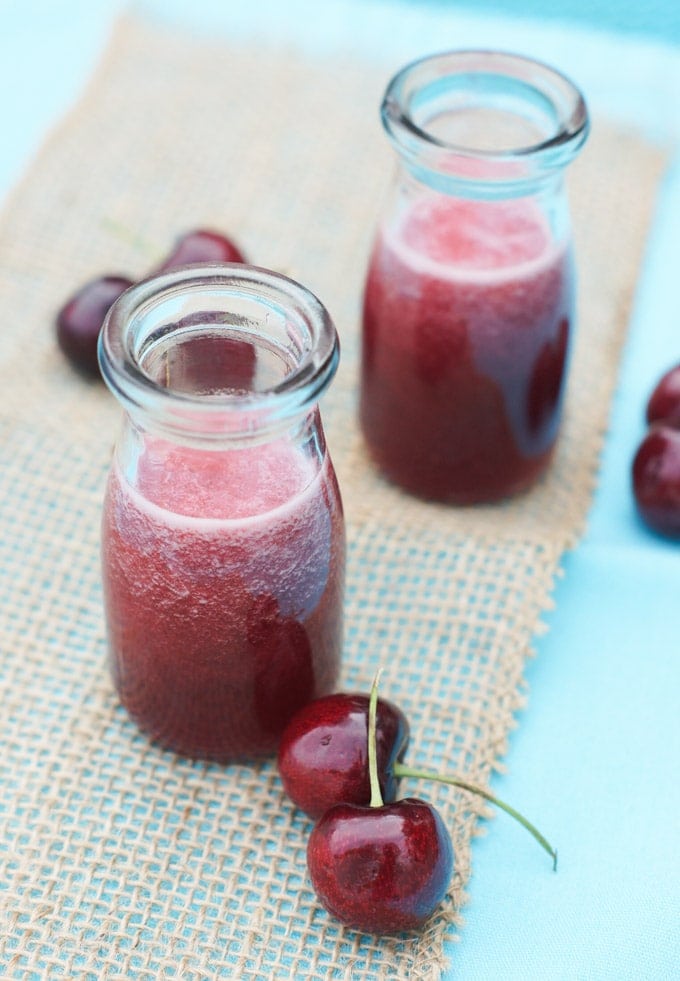 Two glass bottles with simple syrup next to fresh cherries.