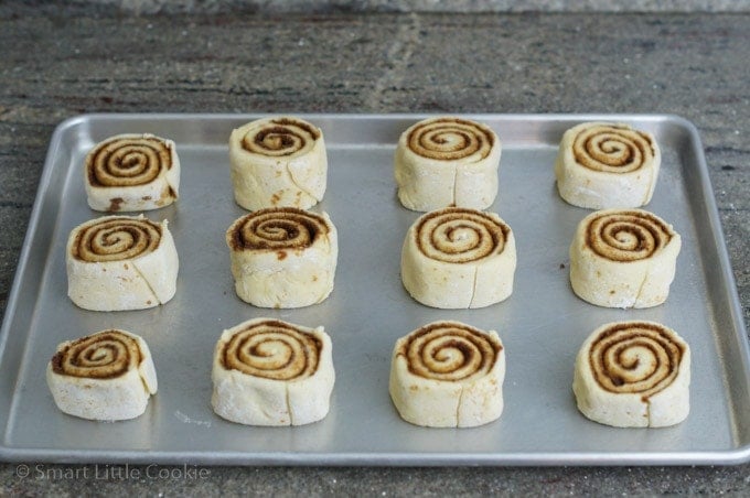 Twelve cinnamon rolls on a baking sheet before being cooked.