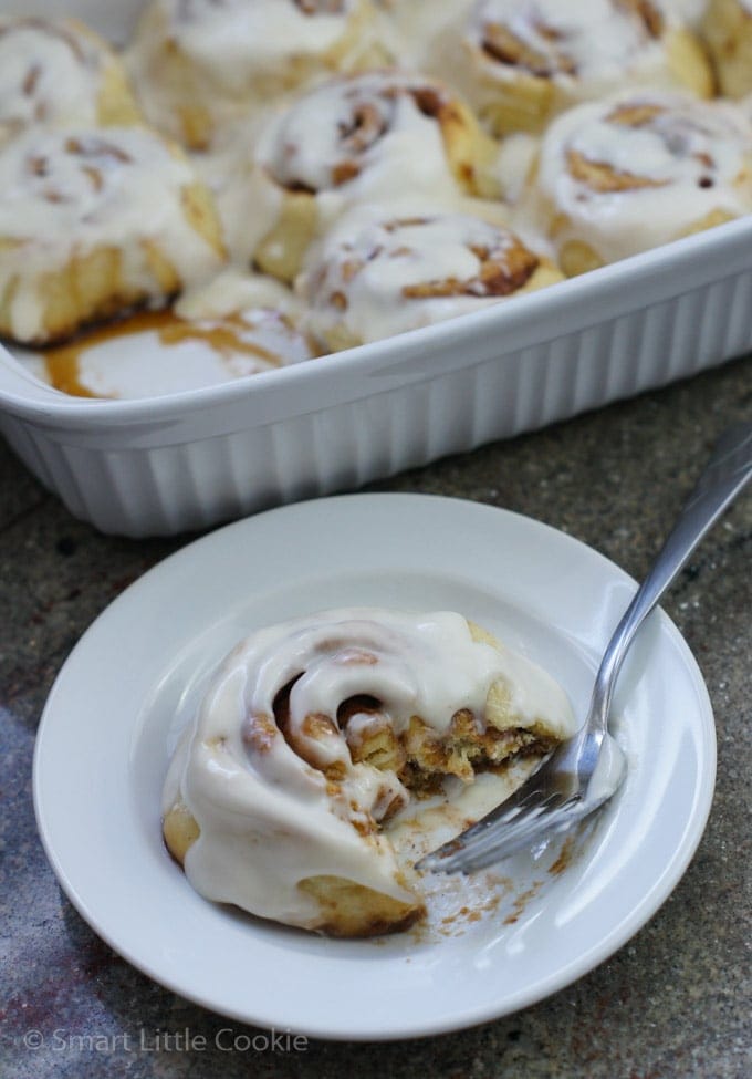 A cinnamon roll in a white bowl with a spoon.