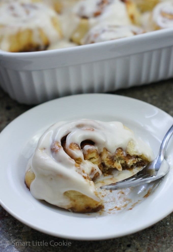 A cinnamon roll in a white bowl being eaten with a fork.