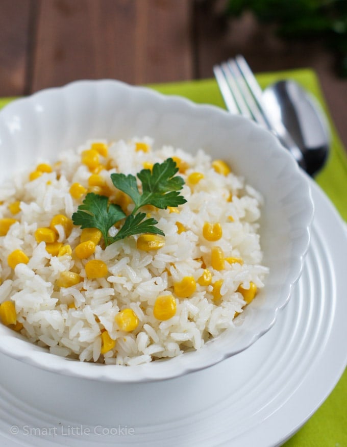 Arroz con Maíz servido en un plato blanco y cubierto con una hoja de perejil. 