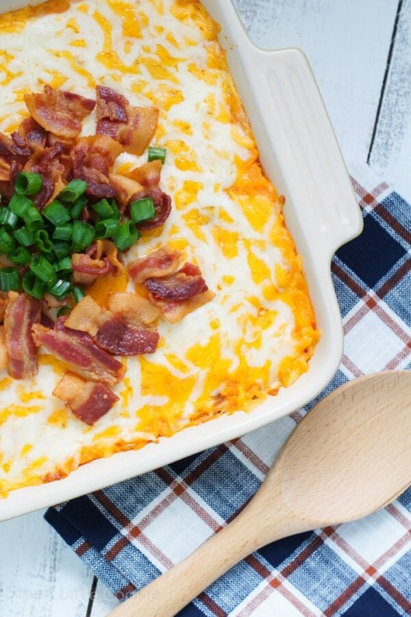 A loaded sweet potato casserole in a baking dish next to a wooden spoon.