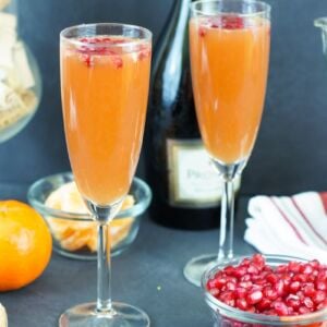 Two tangerine pomegranate mimosas served in flue glasses next to a bowl of pomegranate seeds.