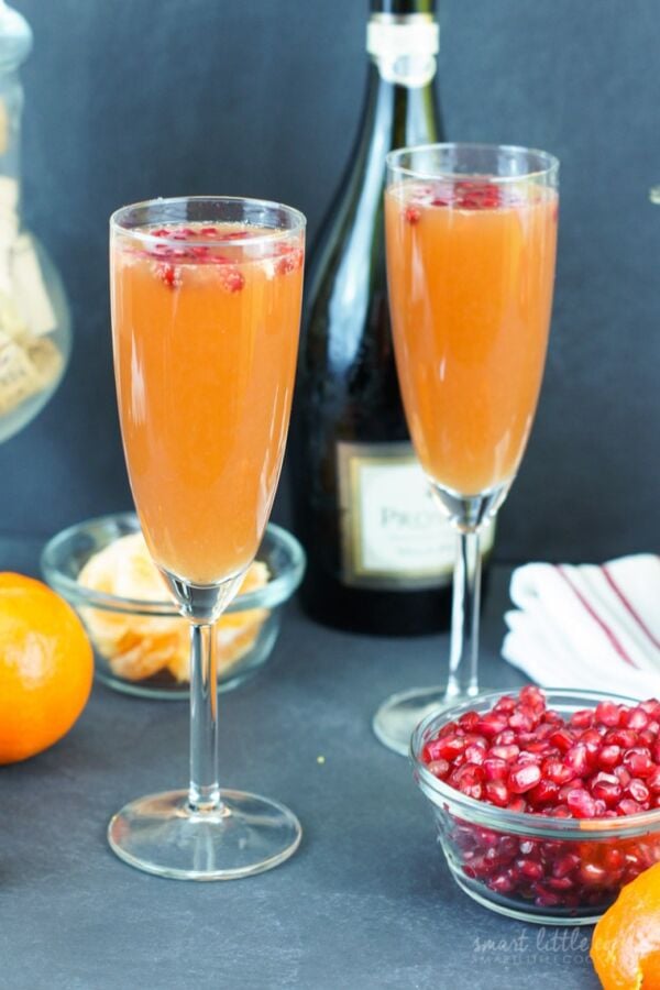 Two tangerine pomegranate mimosas served in flue glasses next to a bowl of pomegranate seeds.