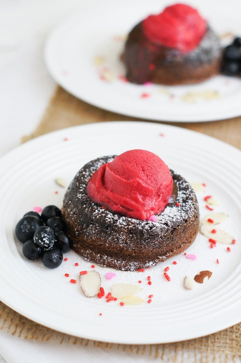 chocolate molten lava cake on a white plate topped with raspberry sorbet and blueberries on the side