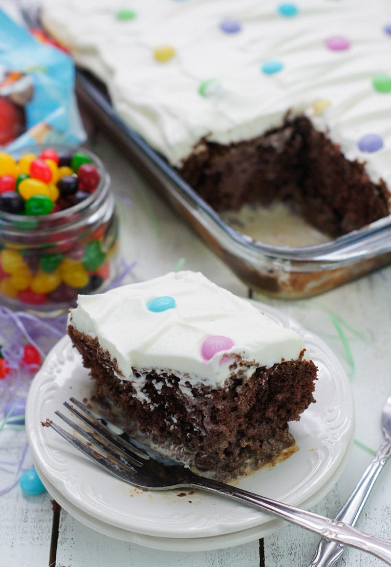 Close up of a square of frosted chocolate cake on a plate with a fork.