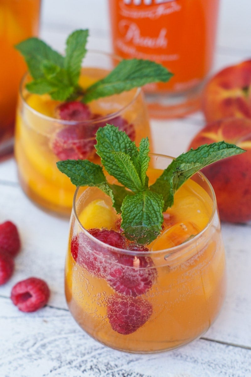 Two glasses of the peach spritzer with fresh raspberries and mint garnish.