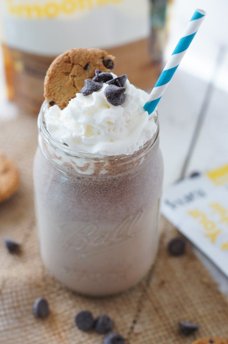 A chocolate chip cookie smoothie in a glass jar topped with whipped cream, chocolate chips and a cookie.