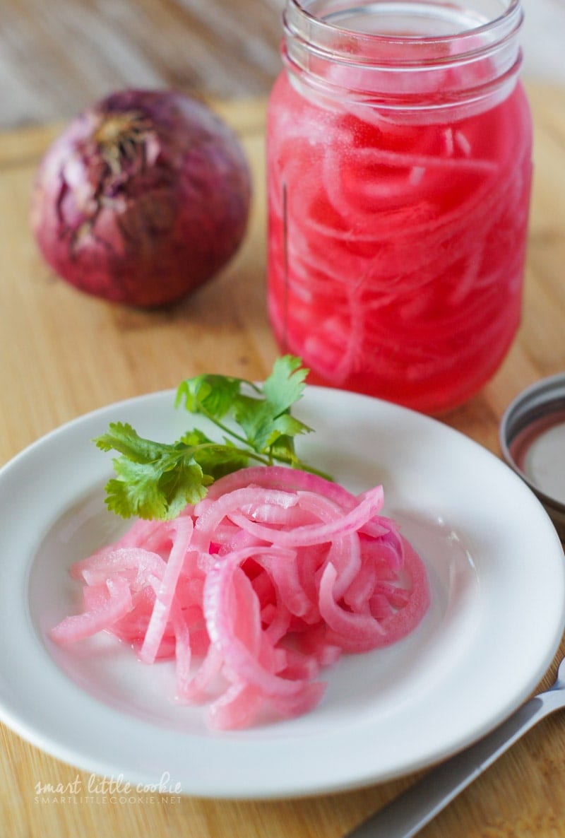 Pickled sliced onions on a white plate with a piece of fresh cilantro.