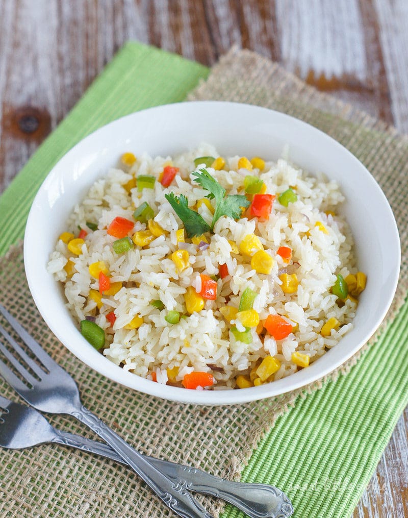 Rice and vegetables served in a white bowl next to two forks.