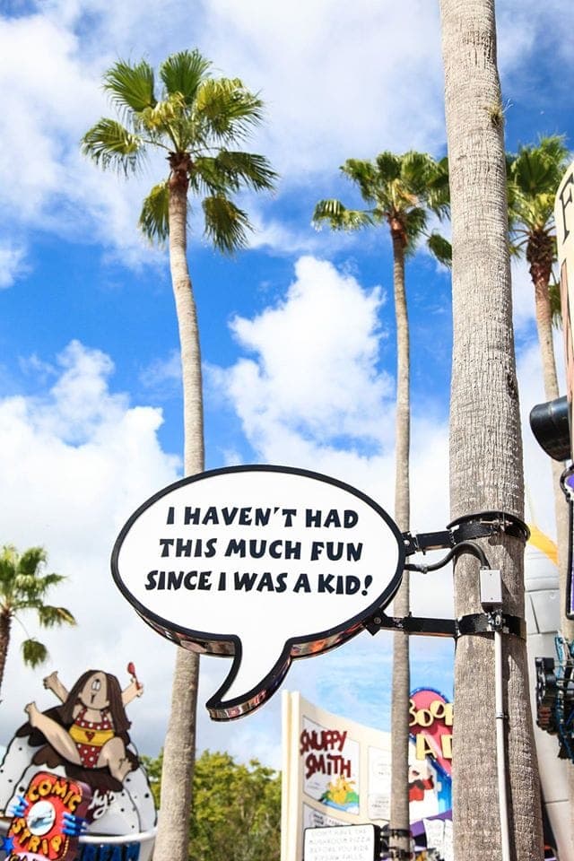 A sign attached to a palm tree saying \'I haven\'t had this much fun since I was a kid!\'.