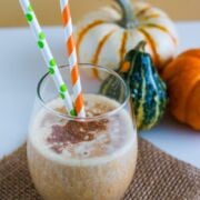 A pumpkin pie smoothie in a glass with two straws.