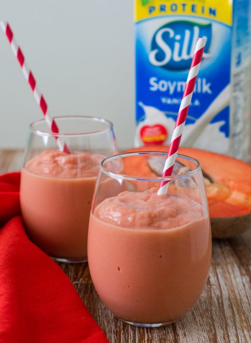 Two glasses of smoothie in front of a carton of soy milk.