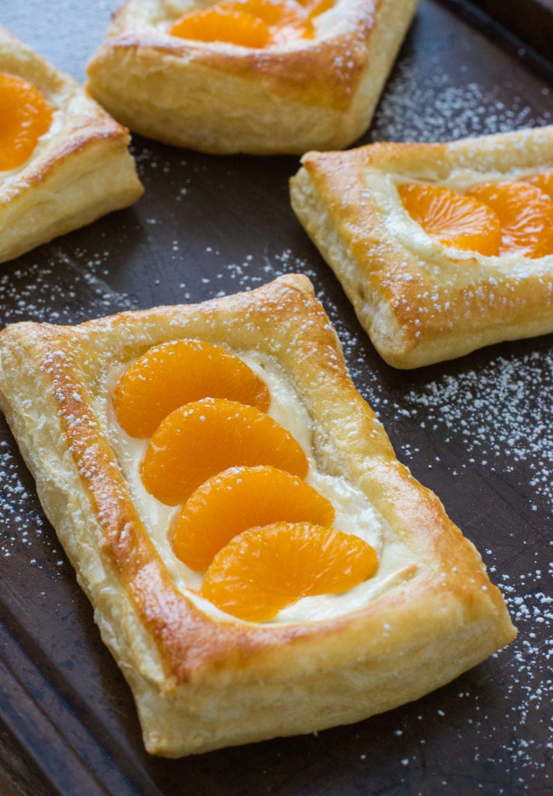 Pastries topped with cream cheese and segments of mandarin.