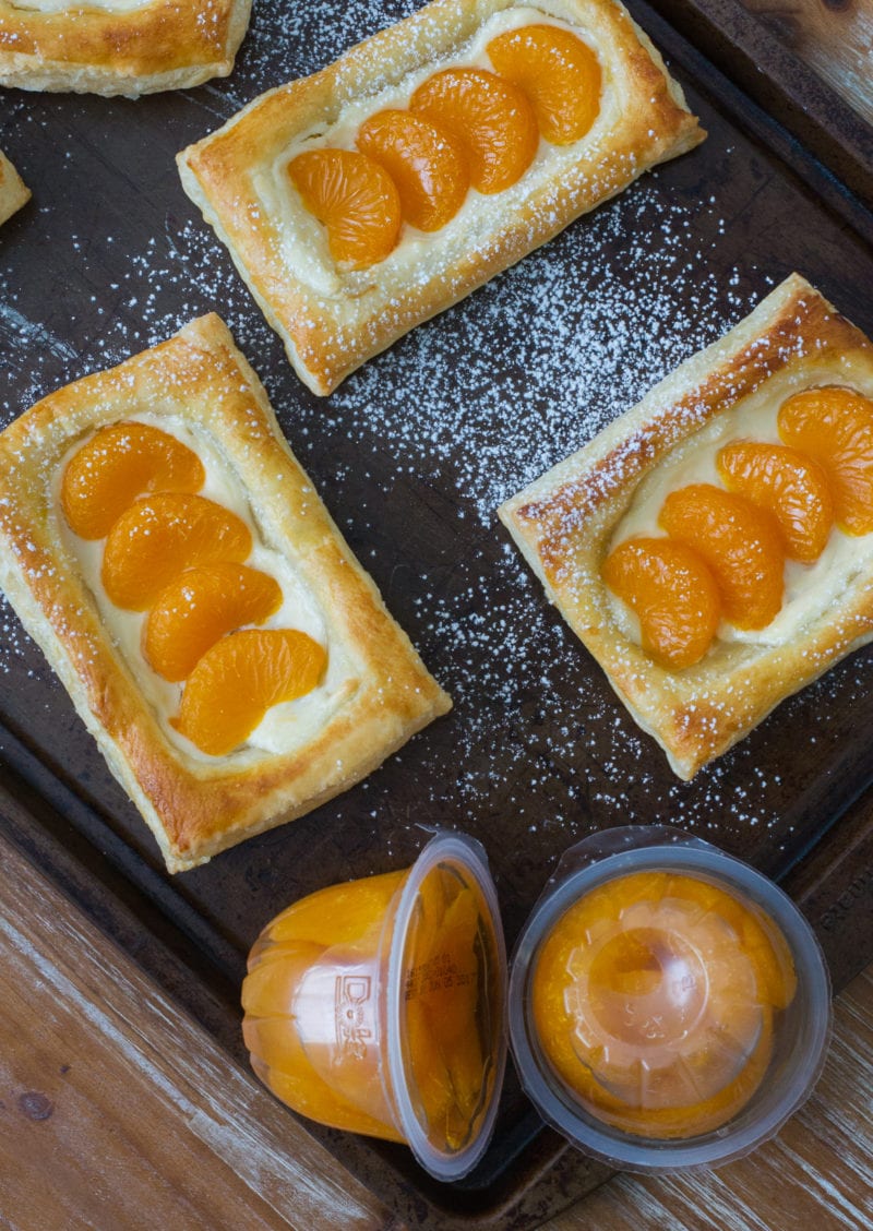 Three pastelitos on a baking sheet next to fruit cups.