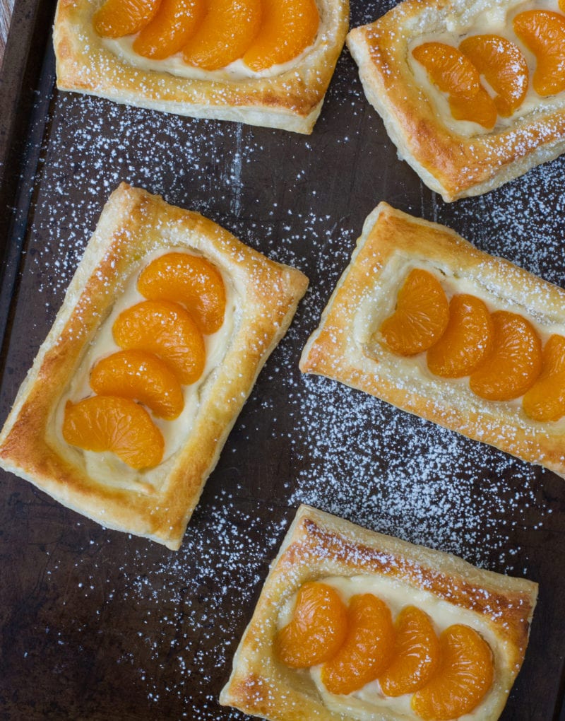 Mandarin and cheese pastelitos on a baking sheet dusted with powdered sugar.