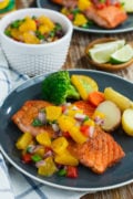 Pan seared salmon topped with peach salsa , served on a blue plate.