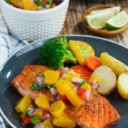 Pan seared salmon topped with peach salsa , served on a blue plate.