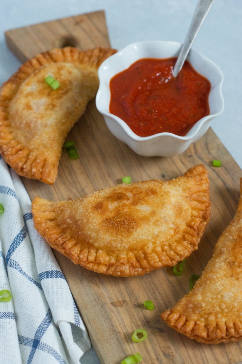 Close up of a chicken parm empanada next to a bowl of red dipping sauce.