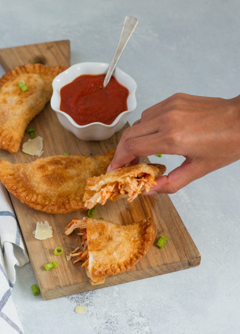 A hand picking up half of an empanada.