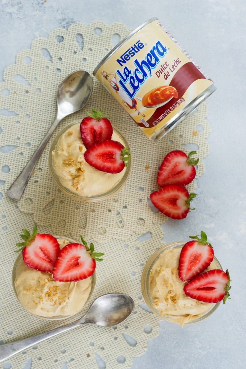 Three dulce leche cheesecakes in jars topped with strawberries.