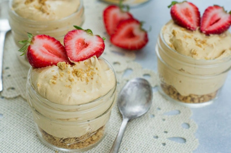 Two jars of no bake cheesecake next to a spoon.