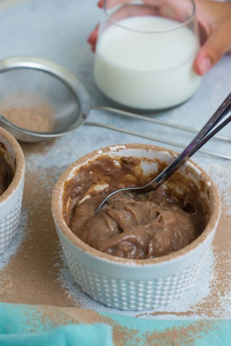 A spoon in a ramekin of chocolate pudding.