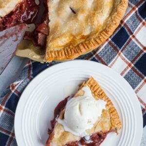 Apple and cranberry pie served with ice cream on a white plate.