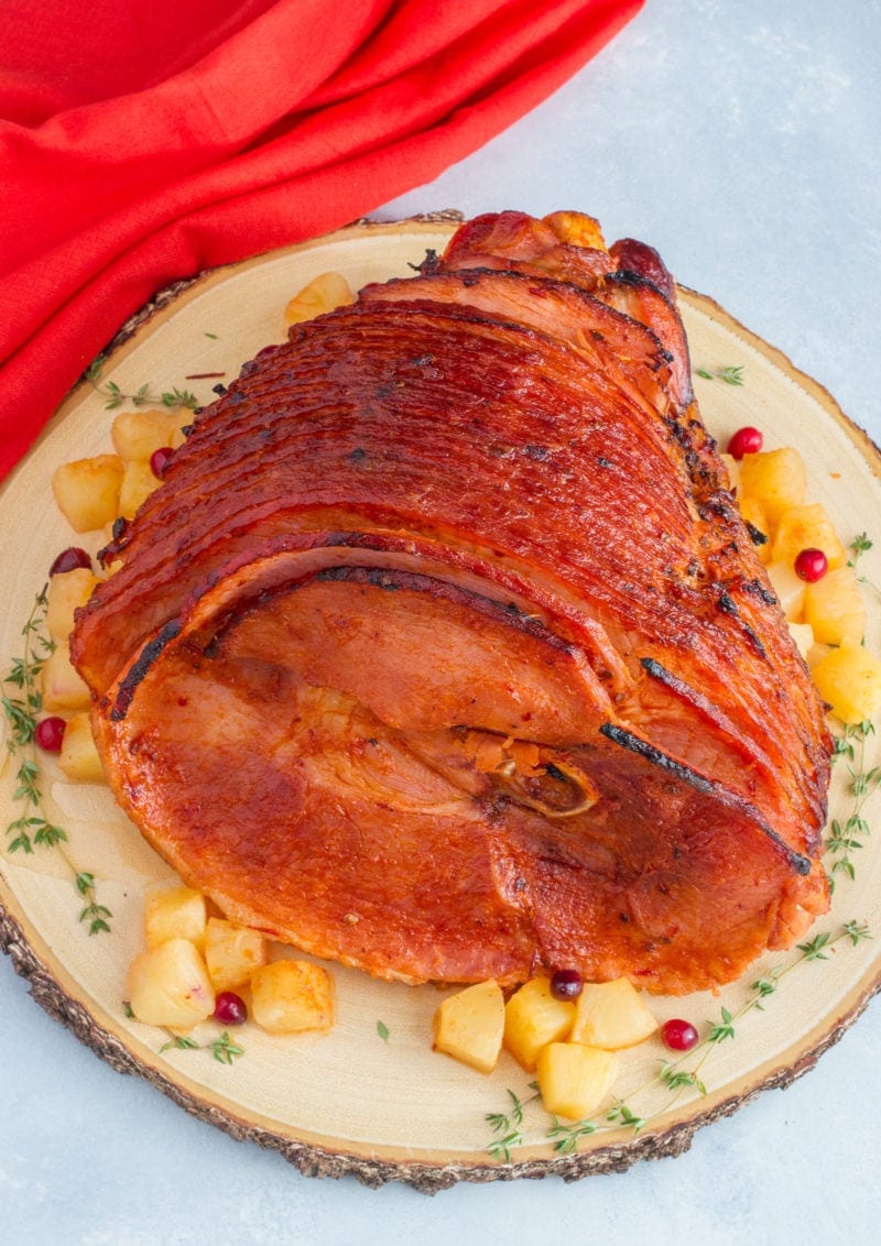 A sliced glazed ham on a plate with chunks of pineapple.