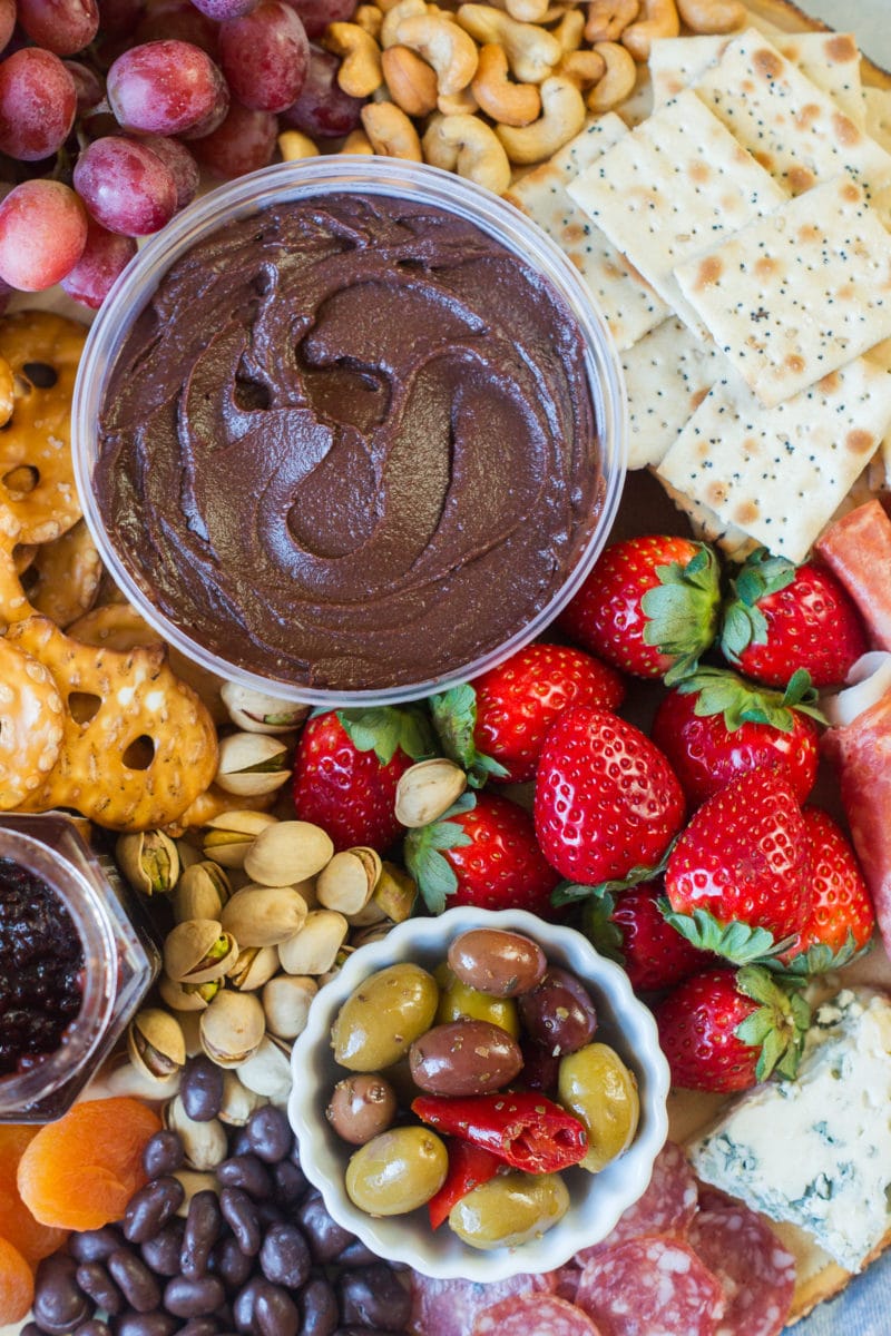 Strawberries next to a bowl of chocolate hummus, crackers and olives.