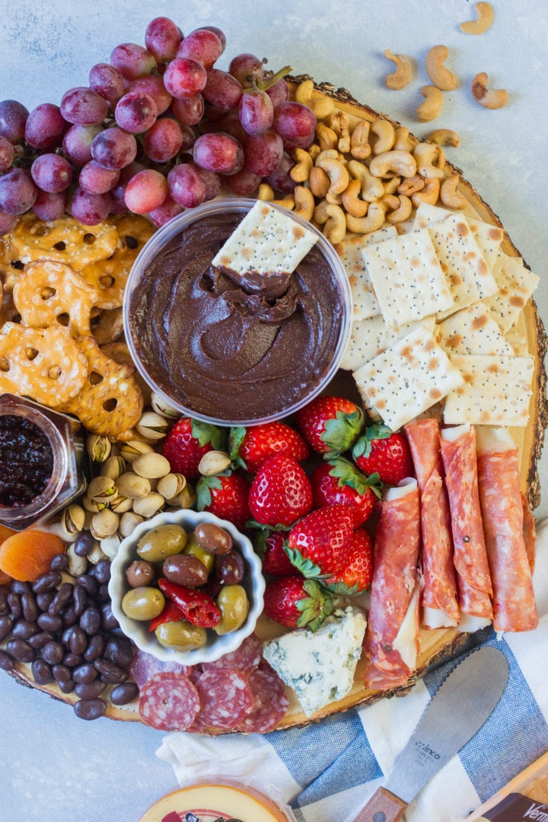 Cheese, ham, fruits, crackers and dips on a platter.