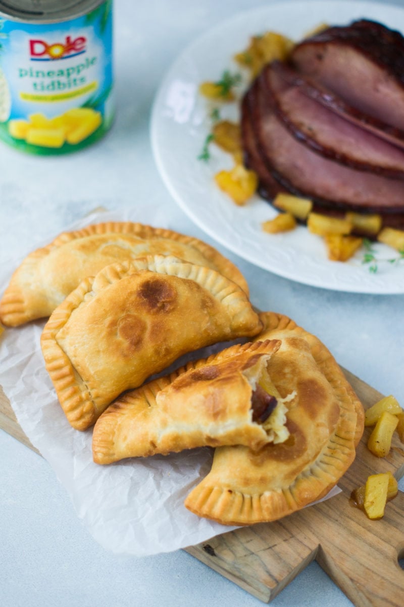 Four empanadas next to slices of glazed ham.