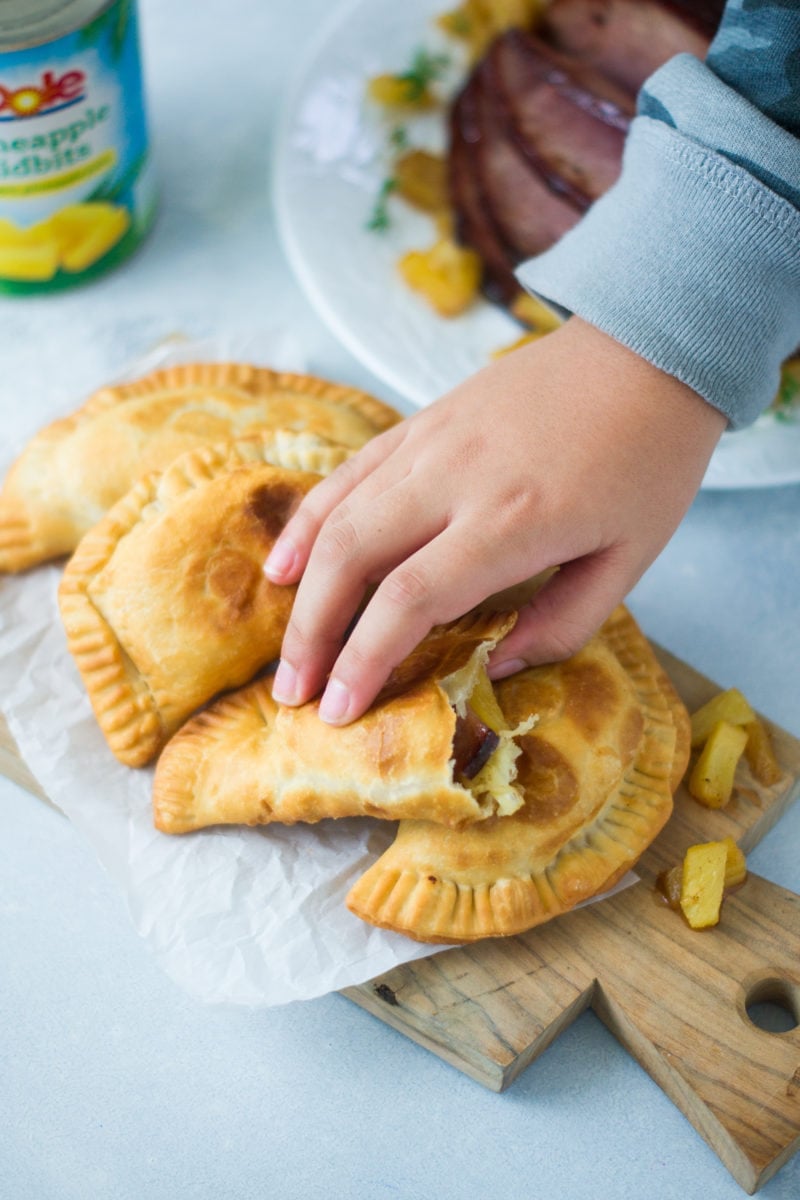 A hand picking up one of the enchiladas from a wooden board.