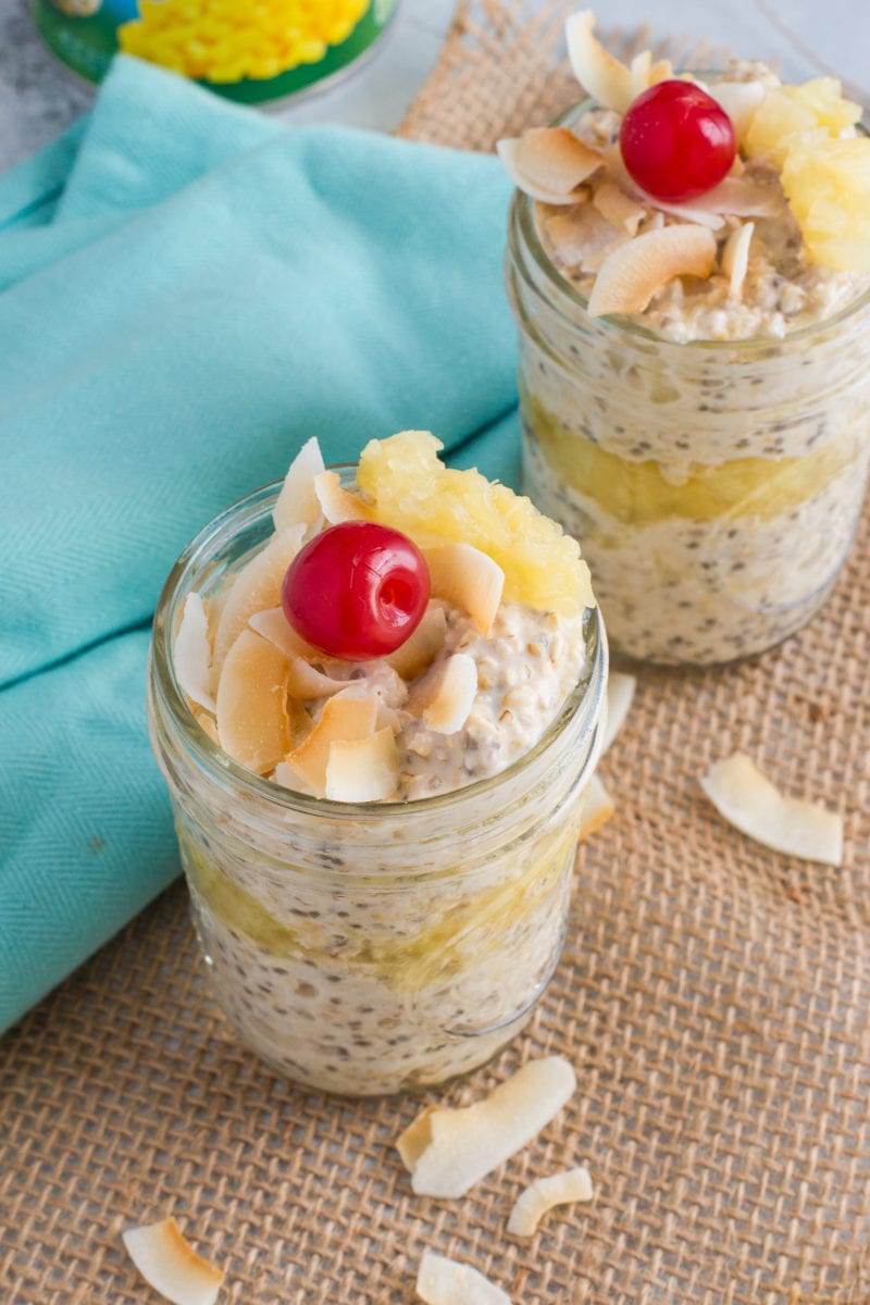 Two jars of oats topped with fresh pineapple and a cherry.
