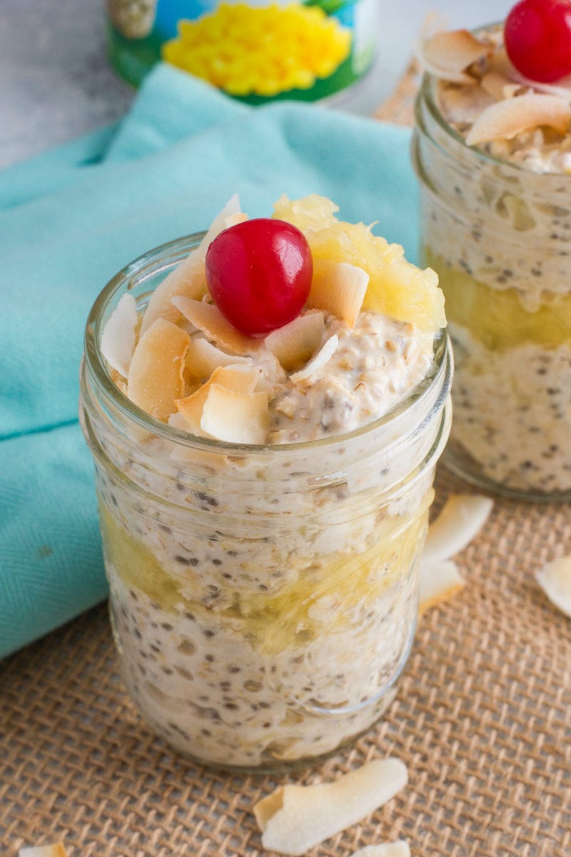 Pina colada overnight oats in a glass jar, topped with a cherry.