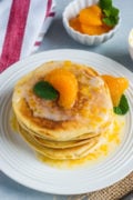 Mascarpone pancakes stacked on a white plate and topped with a mandarin glaze.